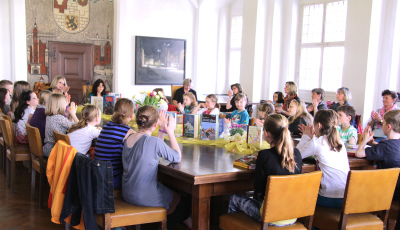 Viele Kinder die um einen großen Tisch herum sitzen, darauf stehen Bücher