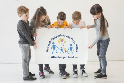 Kinder halten ein Plakat mit dem Logo des Netzwerkes Kinderschutz und Frühe Hilfen