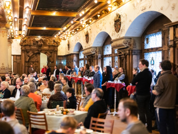 Menschen sitzen oder stehen an Tischen im Bachsaal in festlicher Atmosphäre